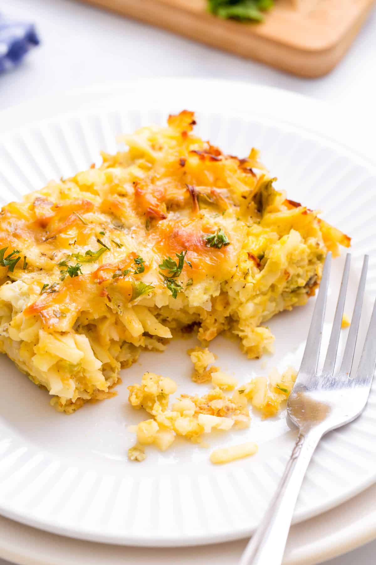 serving of cheesy breakfast potato casserole served on a white round plate with a silver fork