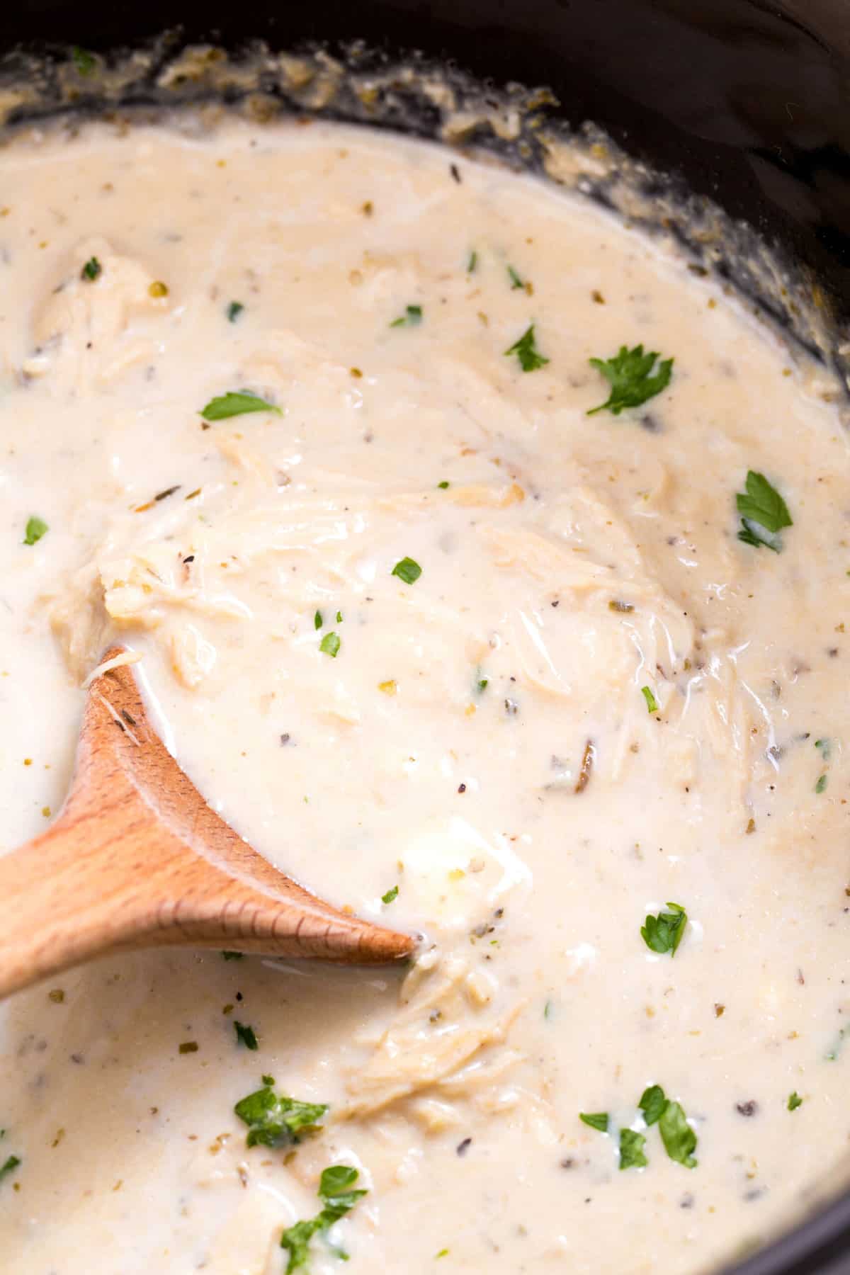 close up image of a wood spoon sitting in a crockpot of creamy chicken
