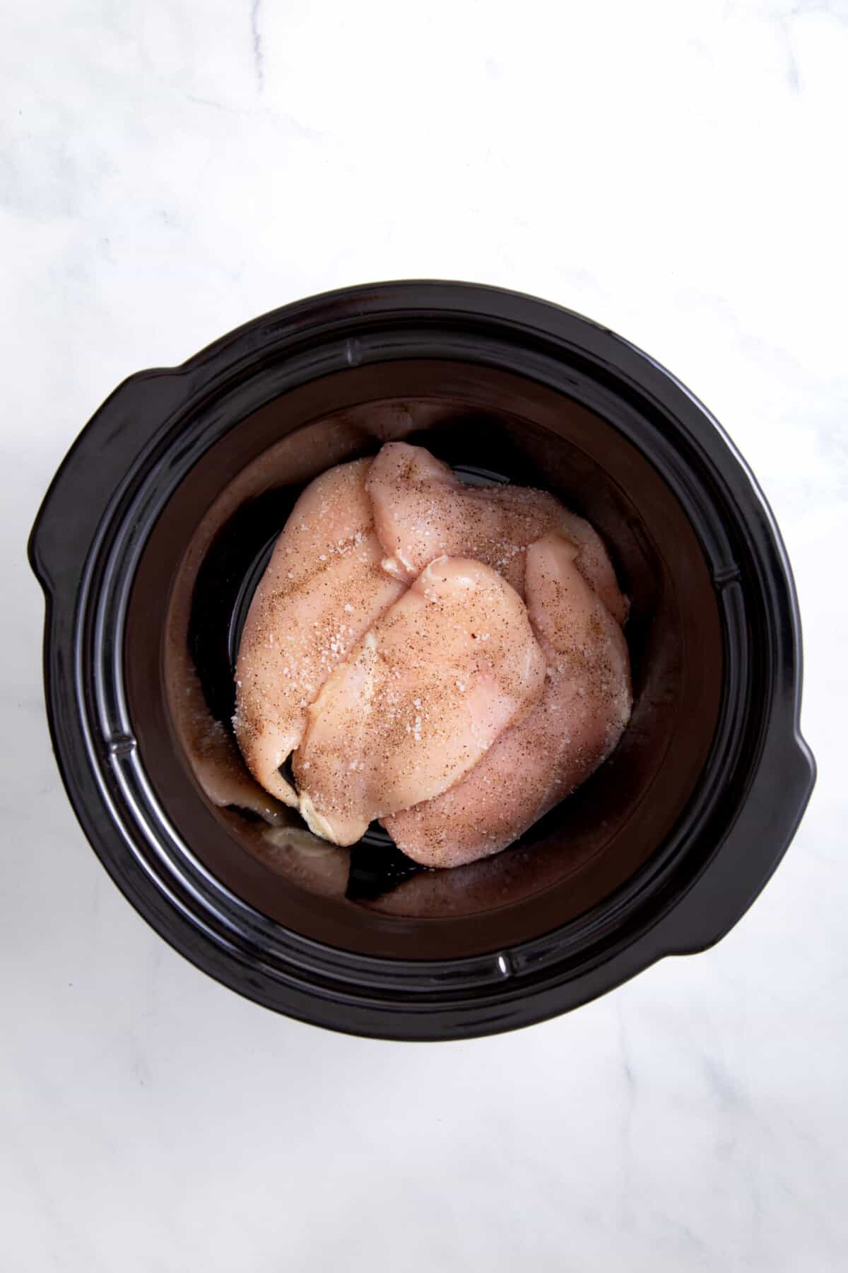 uncooked chicken breasts sitting at the bottom of a crockpot.