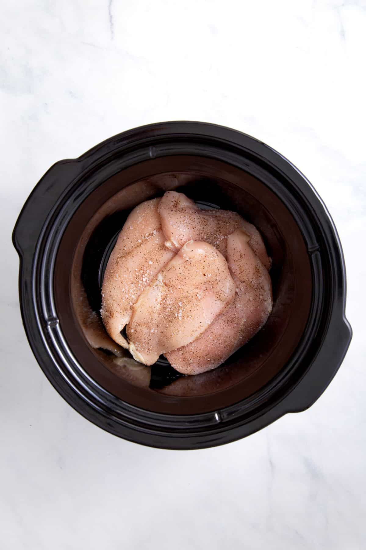 uncooked chicken breasts sitting at the bottom of a crockpot