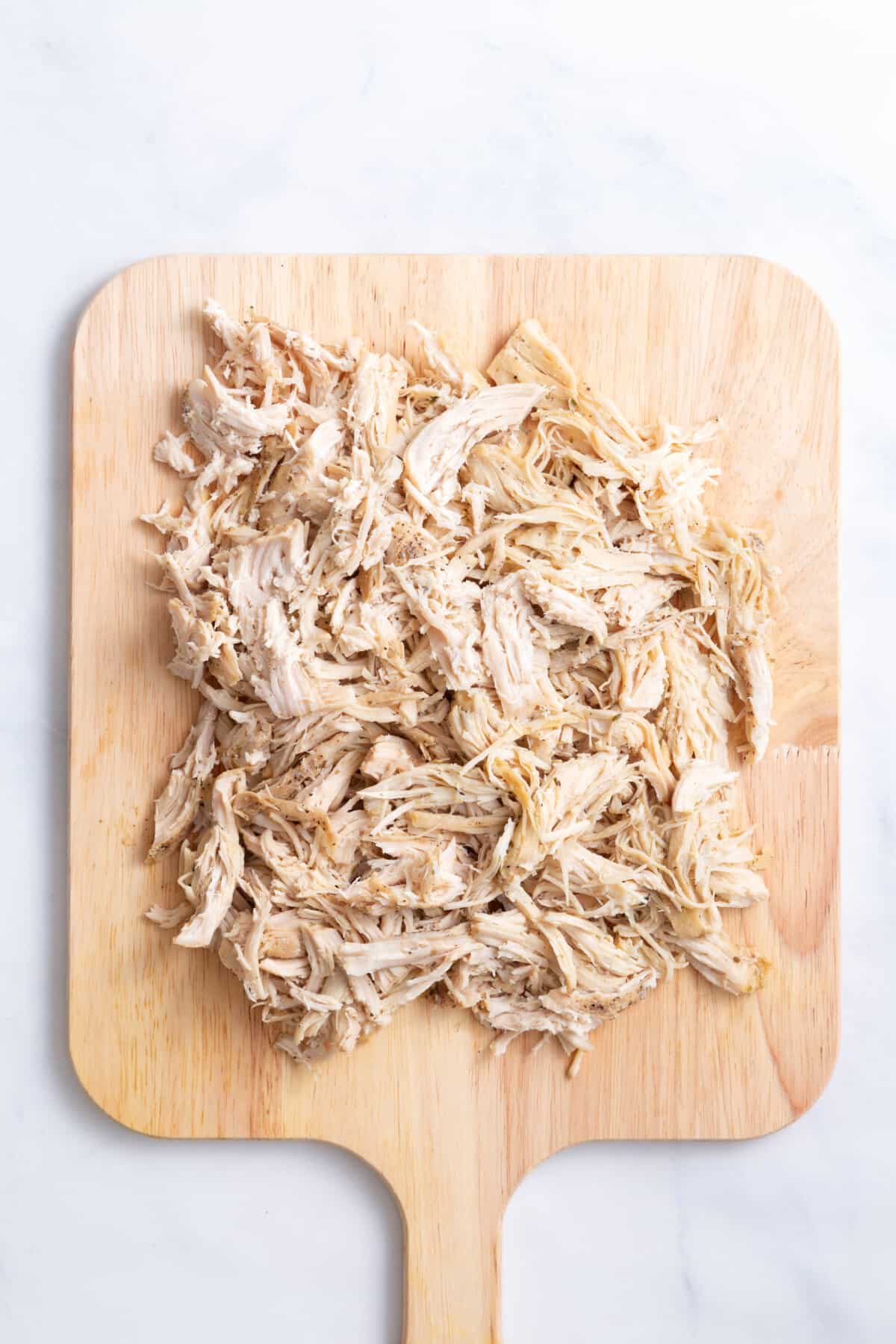 shredded chicken sitting on a wood cutting board.