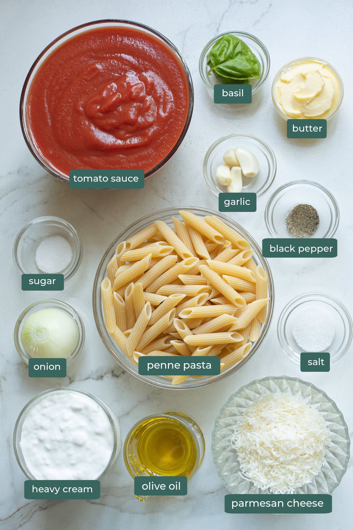 All of the ingredients for creamy tomato basil pasta in bowls on a countertop.