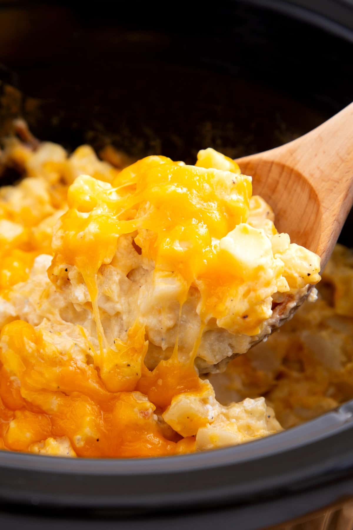 wooden spoonful of cheesy potatoes cooked in a crockpot