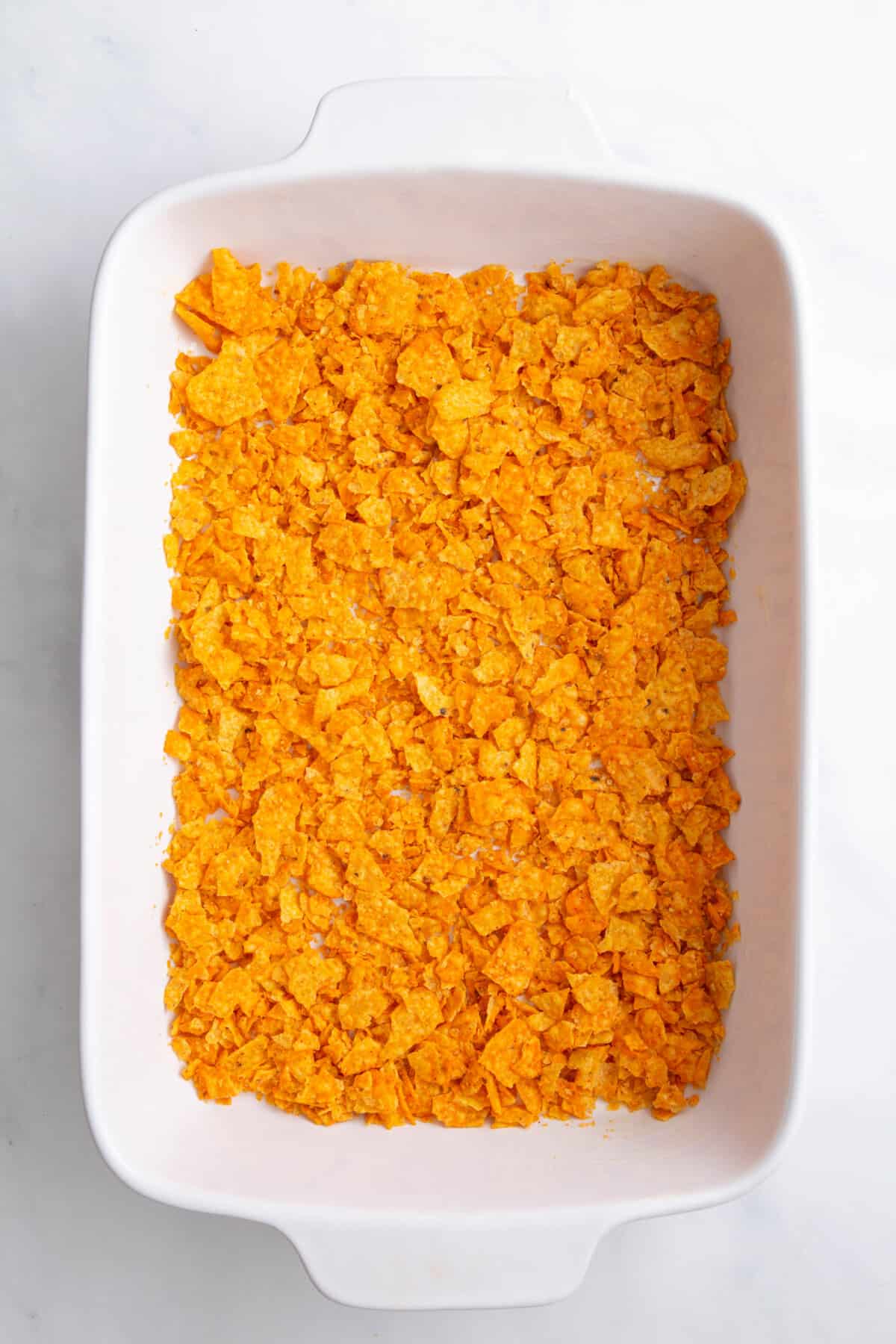 step 1 to make dorito chicken casserole, layer crushed Doritos chips on the bottom of a 9x13 inch casserole dish.