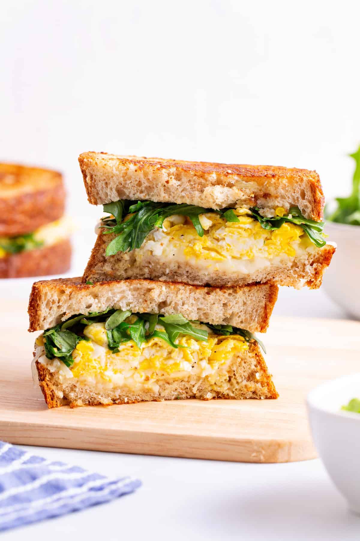 scrambled egg sandwich cut in half and stacked to show the cross section sitting on a wood cutting board