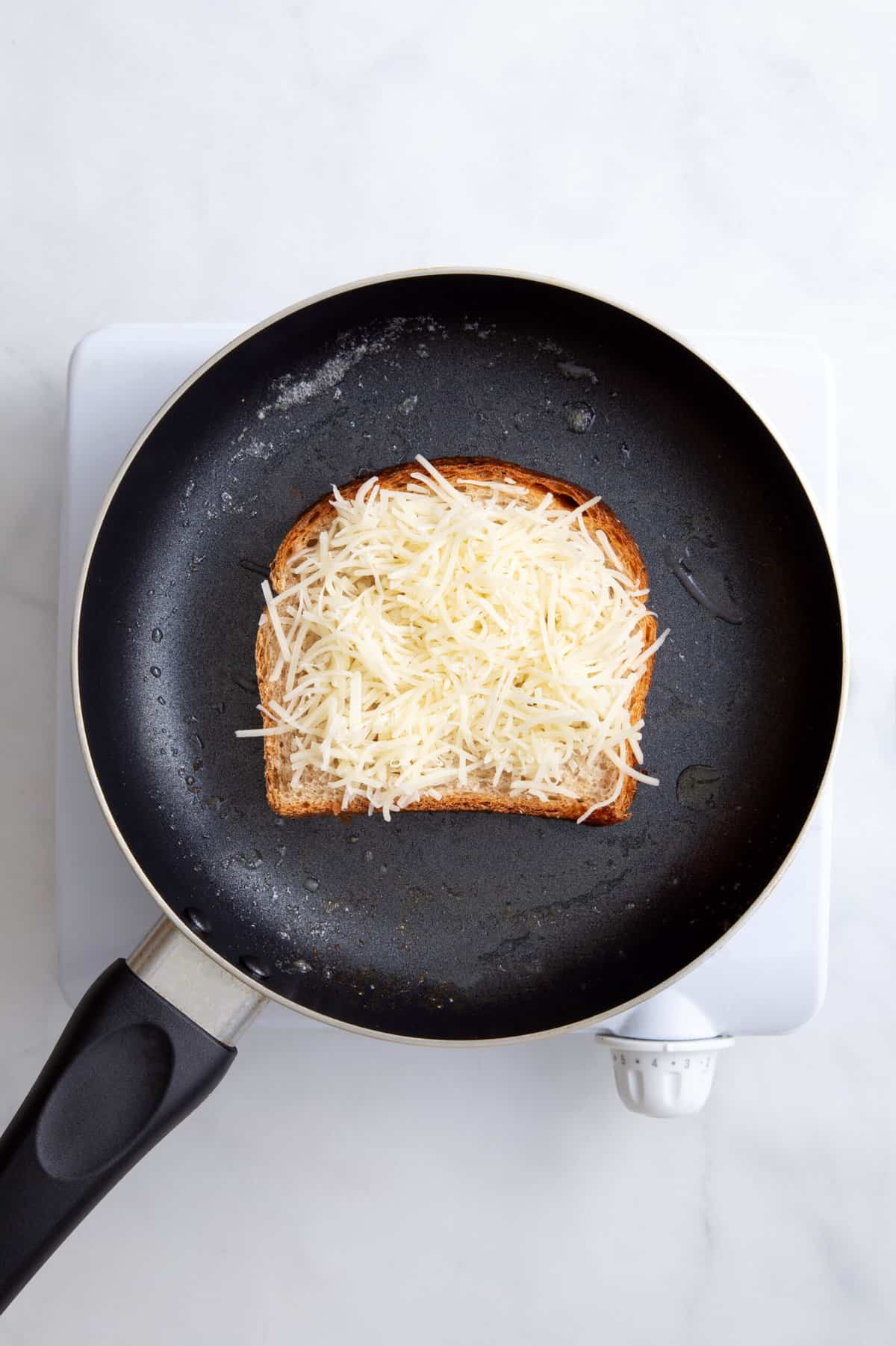 step 1 to make an scrambled egg sandwich, toast a slice of bread with butter on a pan and add shredded cheese on top