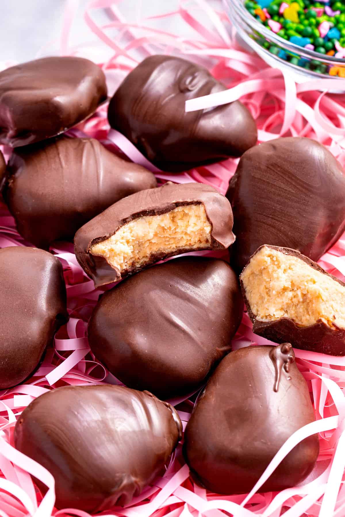 homemade peanut butter eggs sitting in a bed of pink shreds of paper decoration.