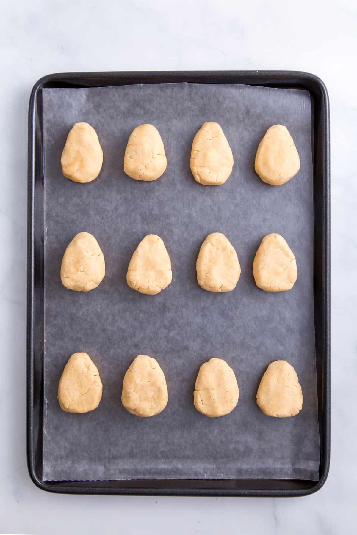 12 peanut butter dessert filling shaped into an egg and lined on a baking tray.