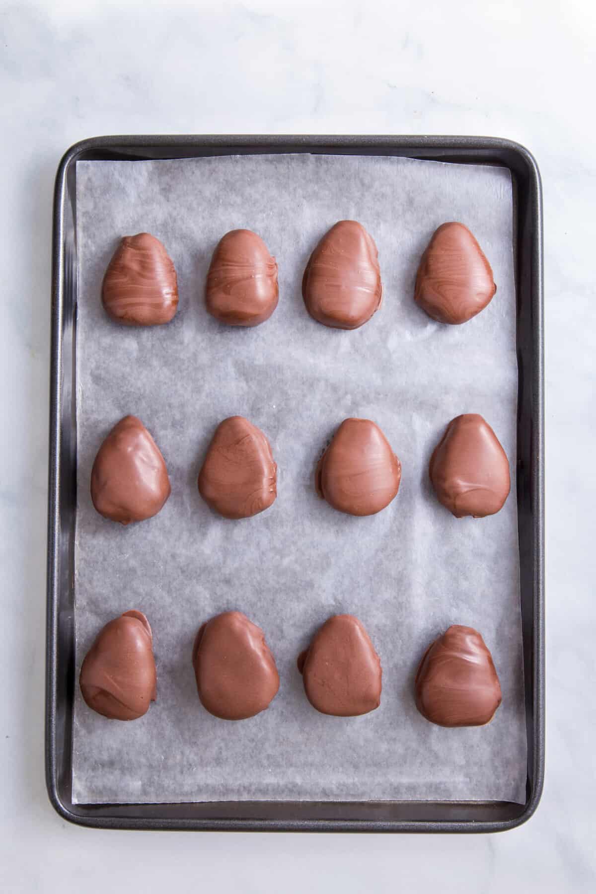 12 chocolate covered peanut butter eggs lined on a baking tray.