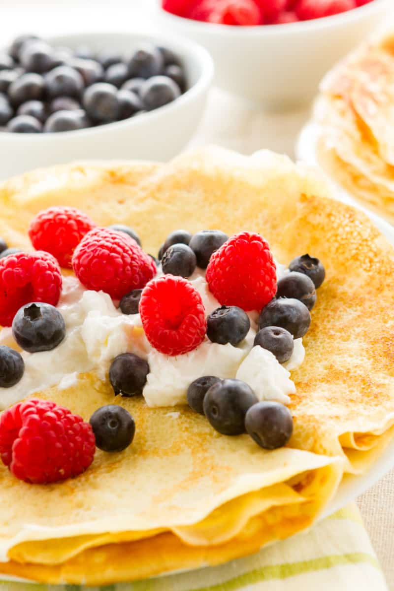 close up image of a plate of homemade crepes with fresh raspberries and blueberries.