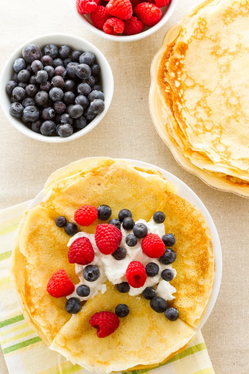 top down image of a plate of crepes topped with fresh berries and whipped cream