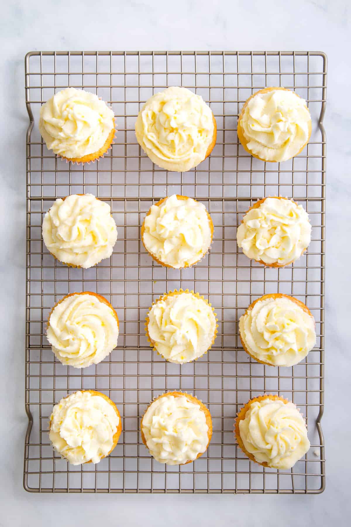12 frosting lemon cupcakes sitting on a wire cooling rack