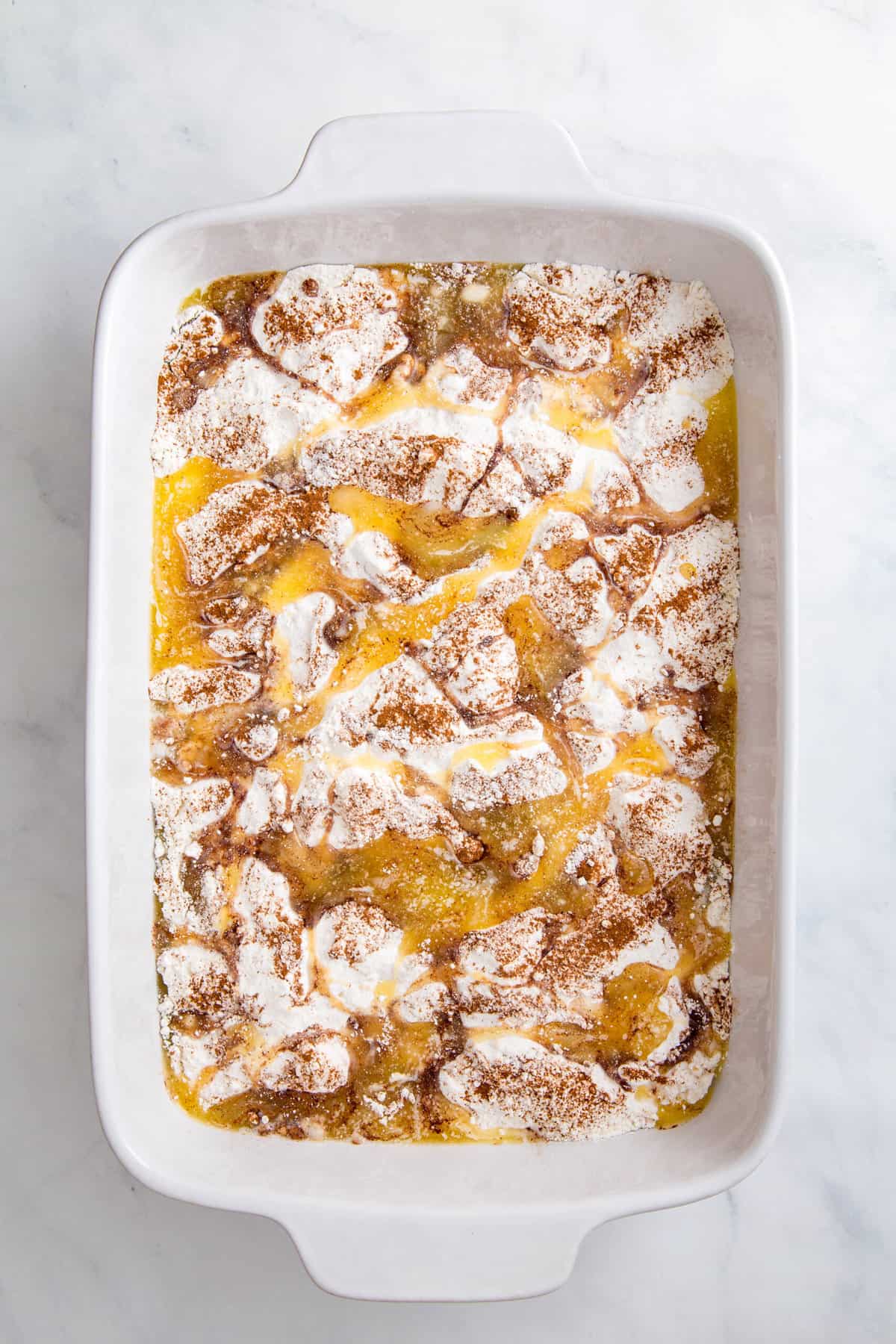 9 by 13 inch casserole dish with canned peaches at the bottom and topped evenly with white cake mix and sprinkled with cinnamon sugar and melted butter