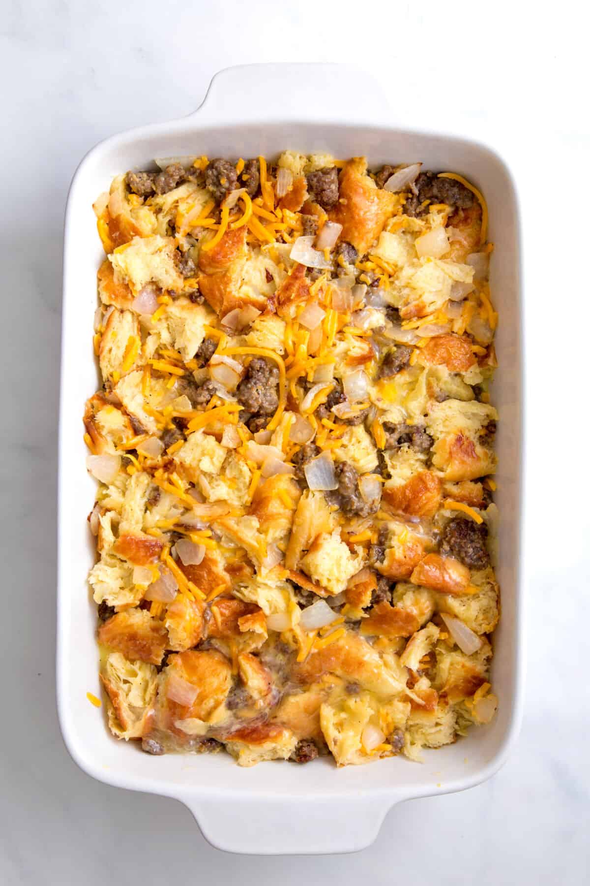 casserole dish with stale pieces of bread and cooked ground pork, onions and shredded cheese and whisked eggs