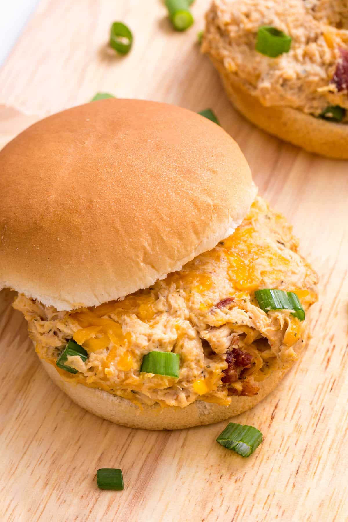 top down close up image of slow cooker crack chicken served between two burger buns sitting on a wood cutting board