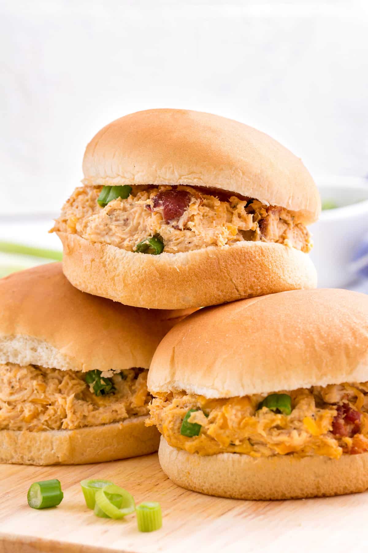 stack of three slow cooker crack chicken sandwiches sitting on a wood cutting board