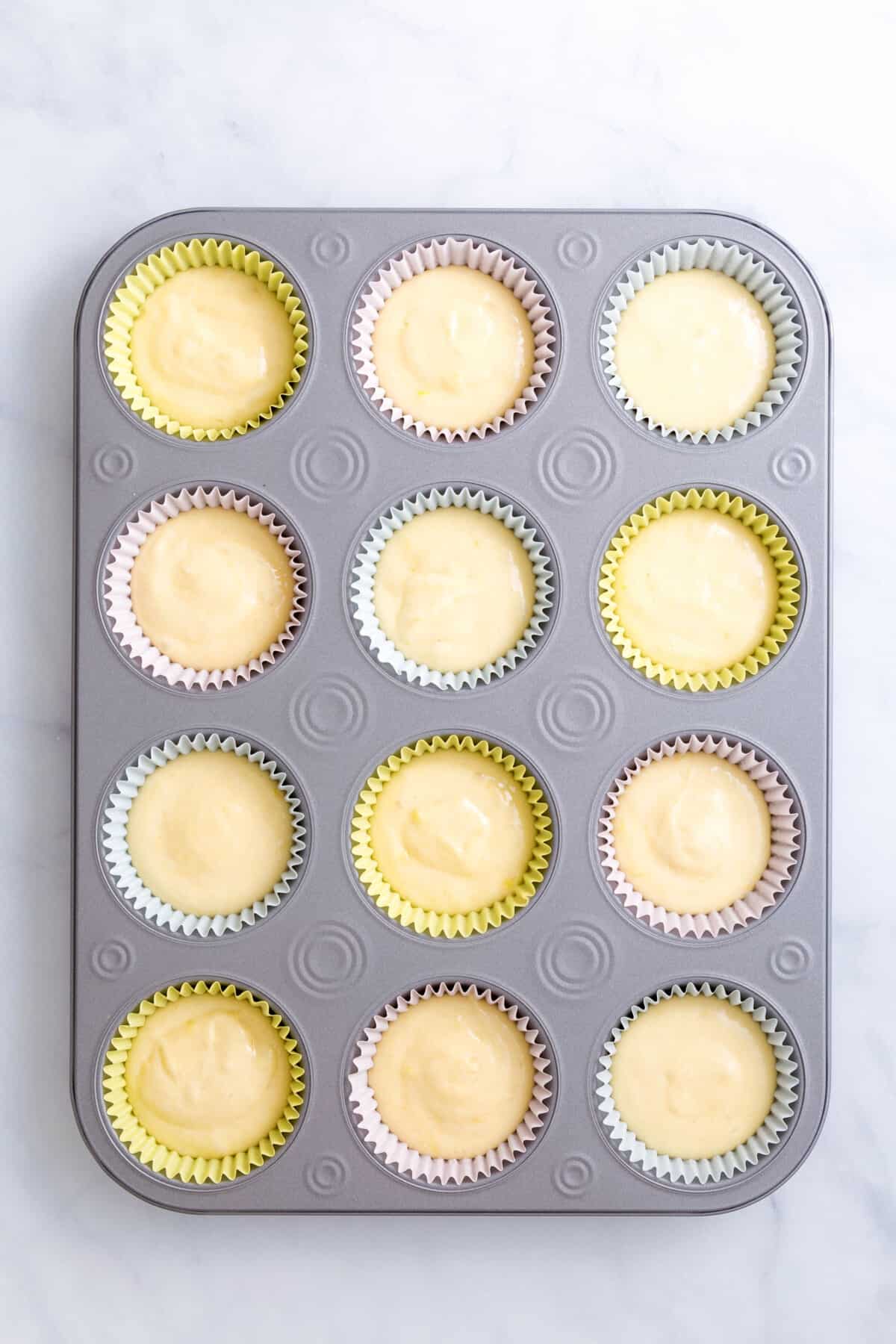 cupcake tin lined with 12 pastel colored cupcake liners with cupcake batter in each slot.