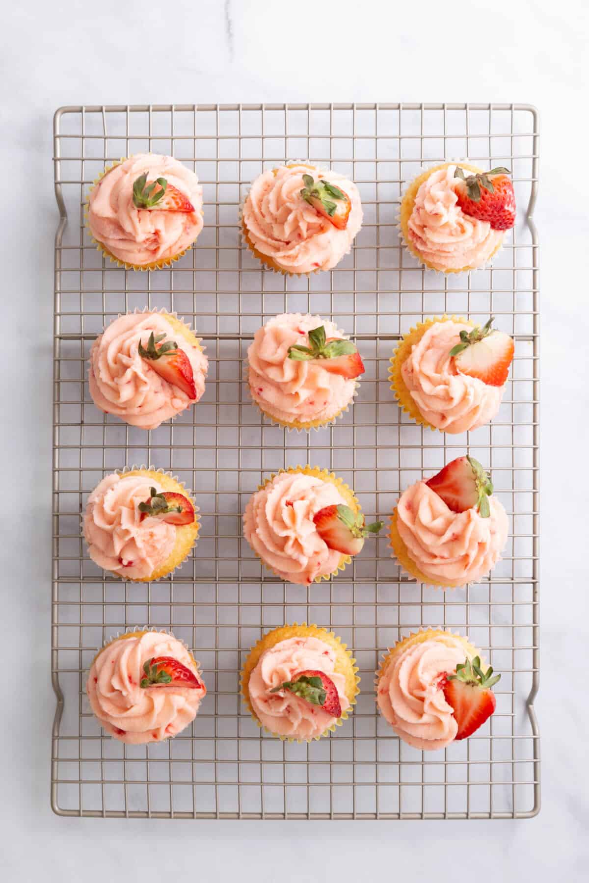 12 lemon strawberry cupcakes cooling on a wire rack.