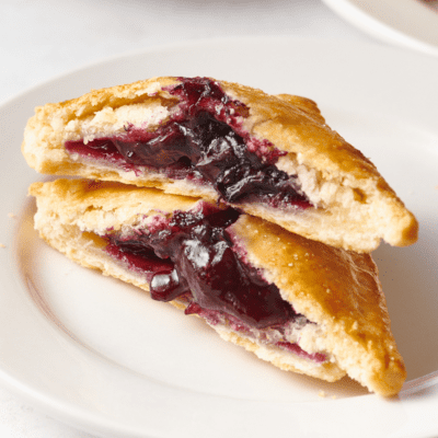 A blueberry hand pie split in half and stacked on a plate.