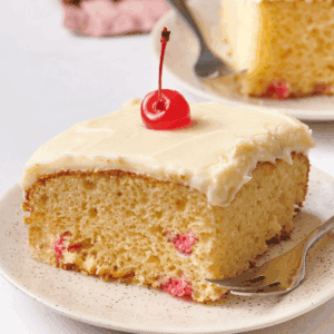 A slice of frosted cherry cake topped with a cherry on a plate.