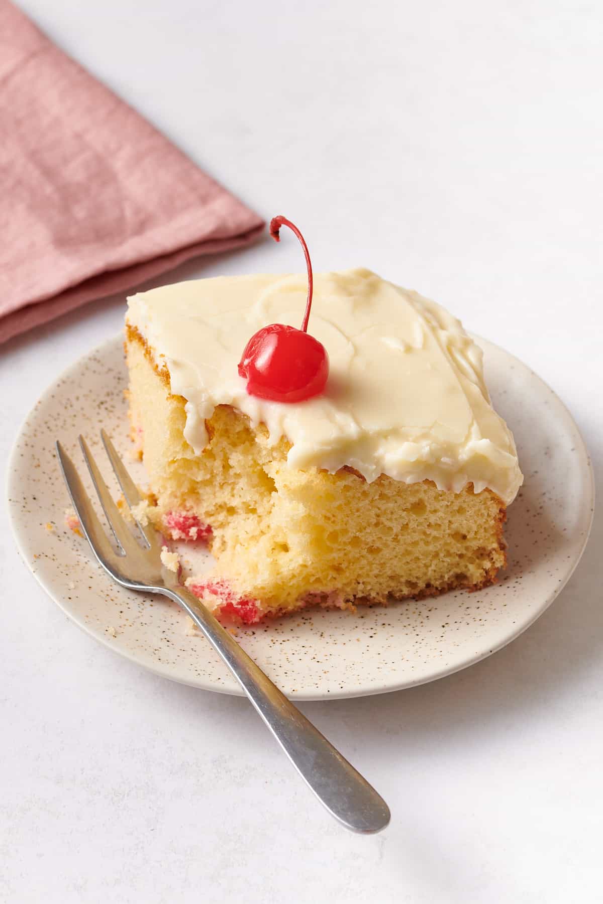 close up image of a square serving of cherry cake served on a speckled beige plate with a silver fork