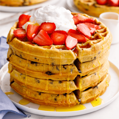 A stack of four chocolate chip waffles topped with strawberries and whipped cream.