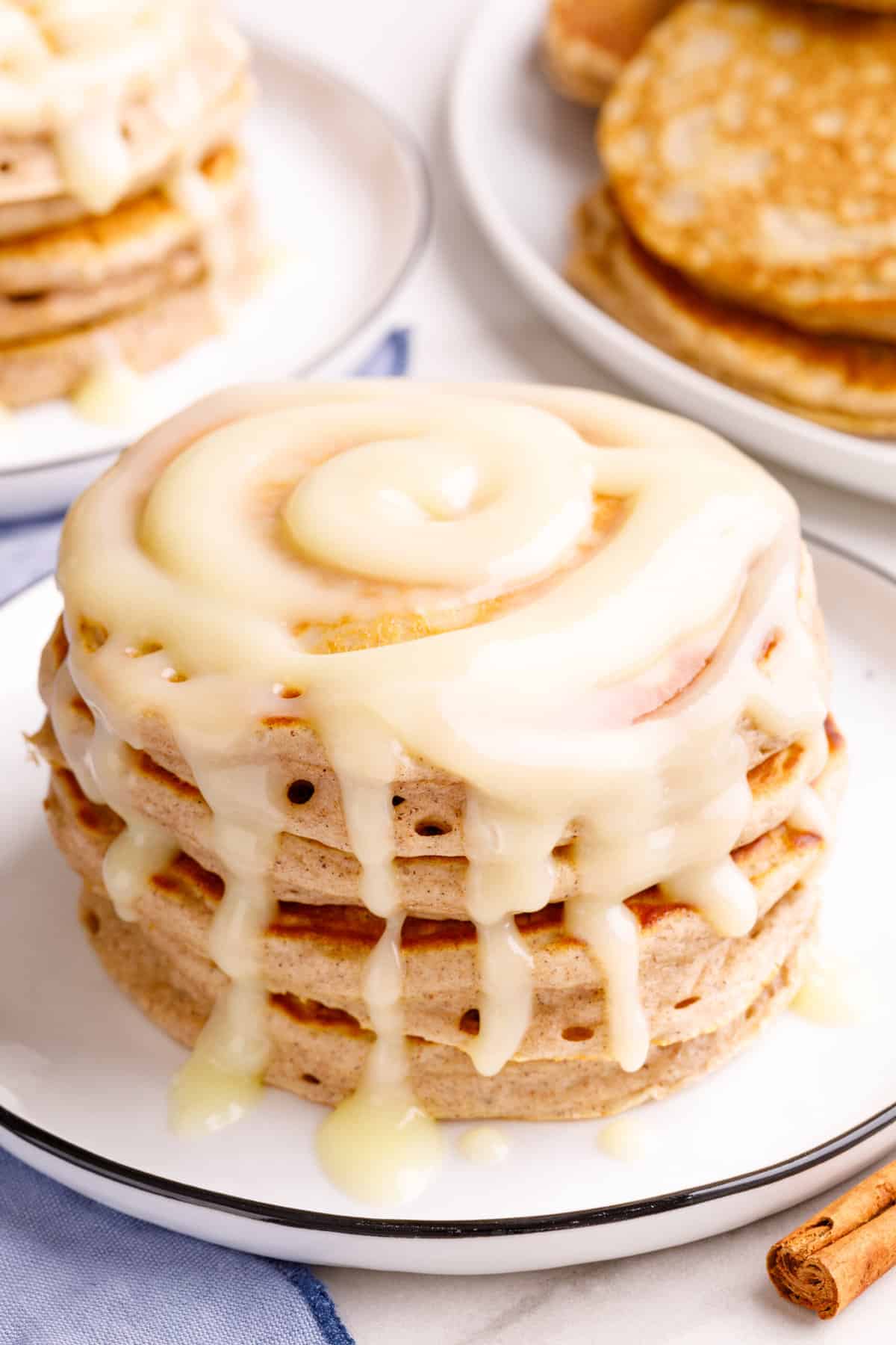 close up image of a stack of four cinnamon pancakes with glaze sitting on a white round plate