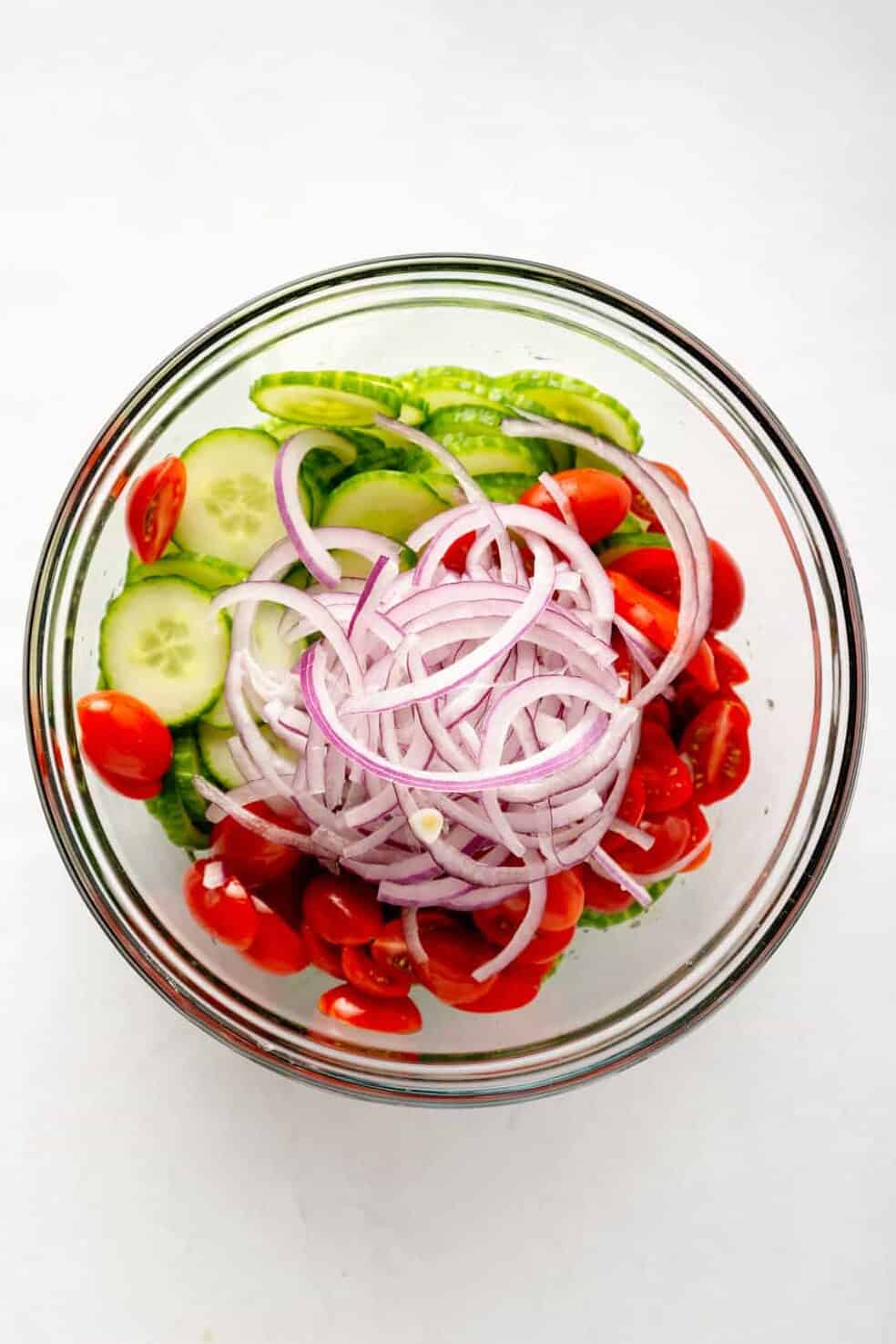 sliced persian cucumbers, cherry tomatoes and red onion in a large glass bowl