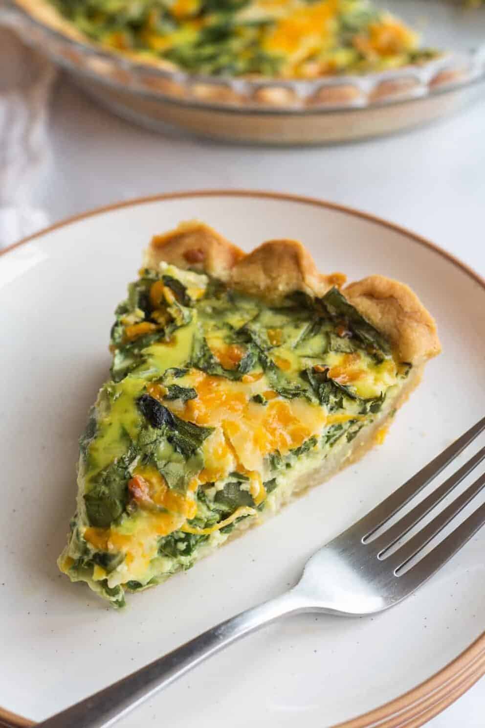 slice of spinach and cheese quiche served on a plate with a silver fork