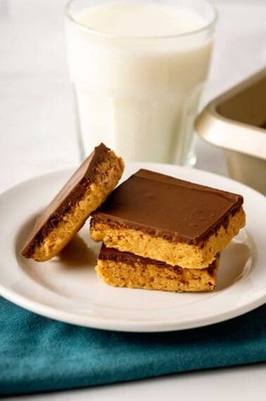 Three no-bake peanut butter bars on a plate with a glass of milk.