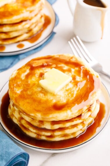 A stack of overnight pancakes on a plate topped with butter and syrup.