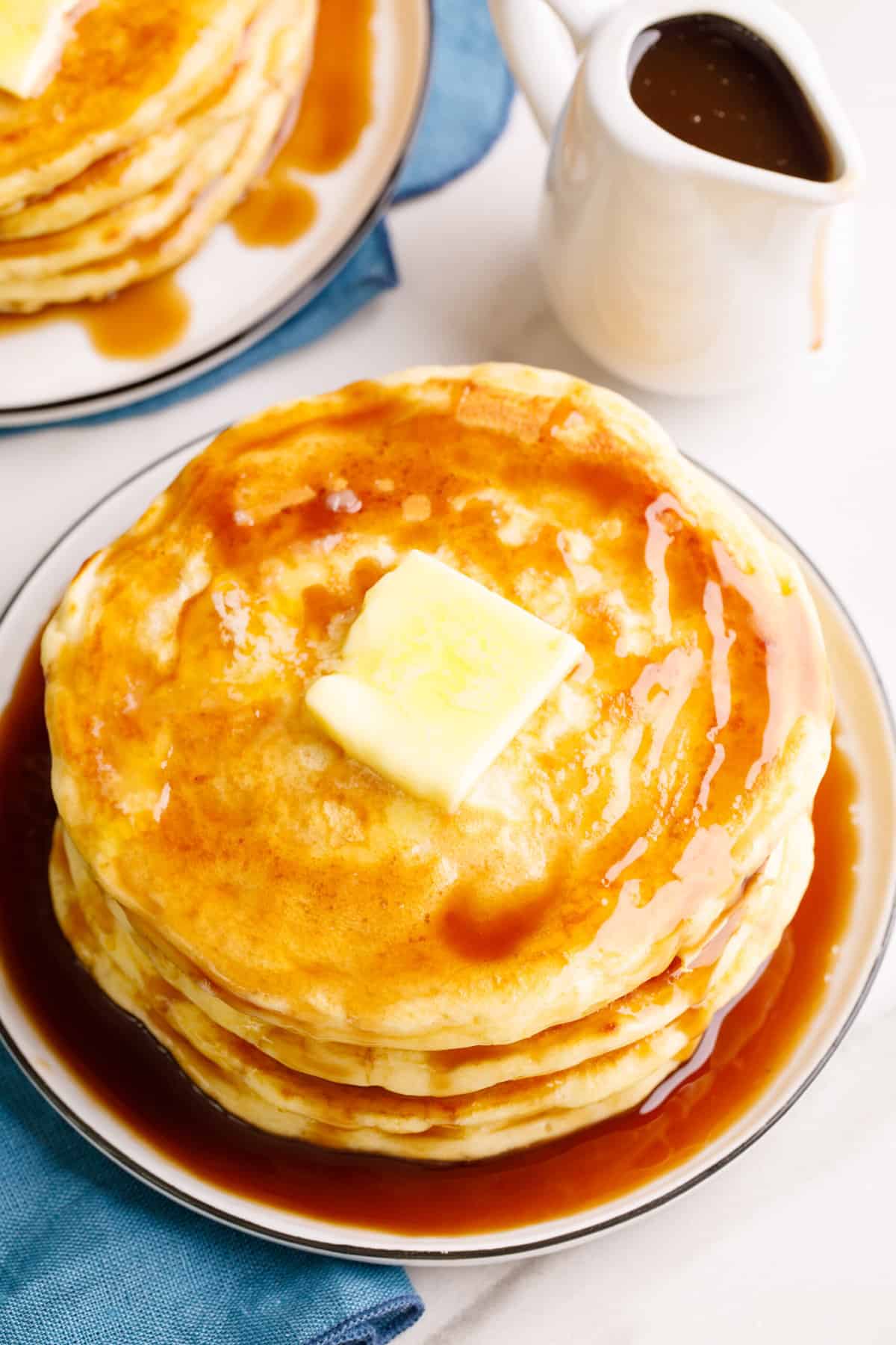 top down image of a stack of four pancakes served on a plate with topped with syrup and butter