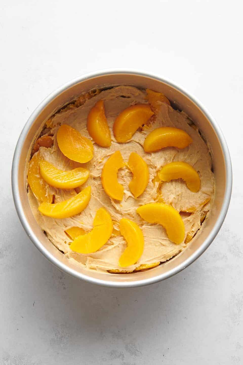 peach cake batter and fresh sliced peaches in a round cake pan