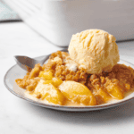 A plate of peach crumble topped with a scoop of vanilla ice cream.