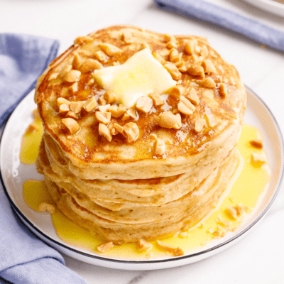 A stack of peanut butter pancakes topped with chopped peanuts and butter.
