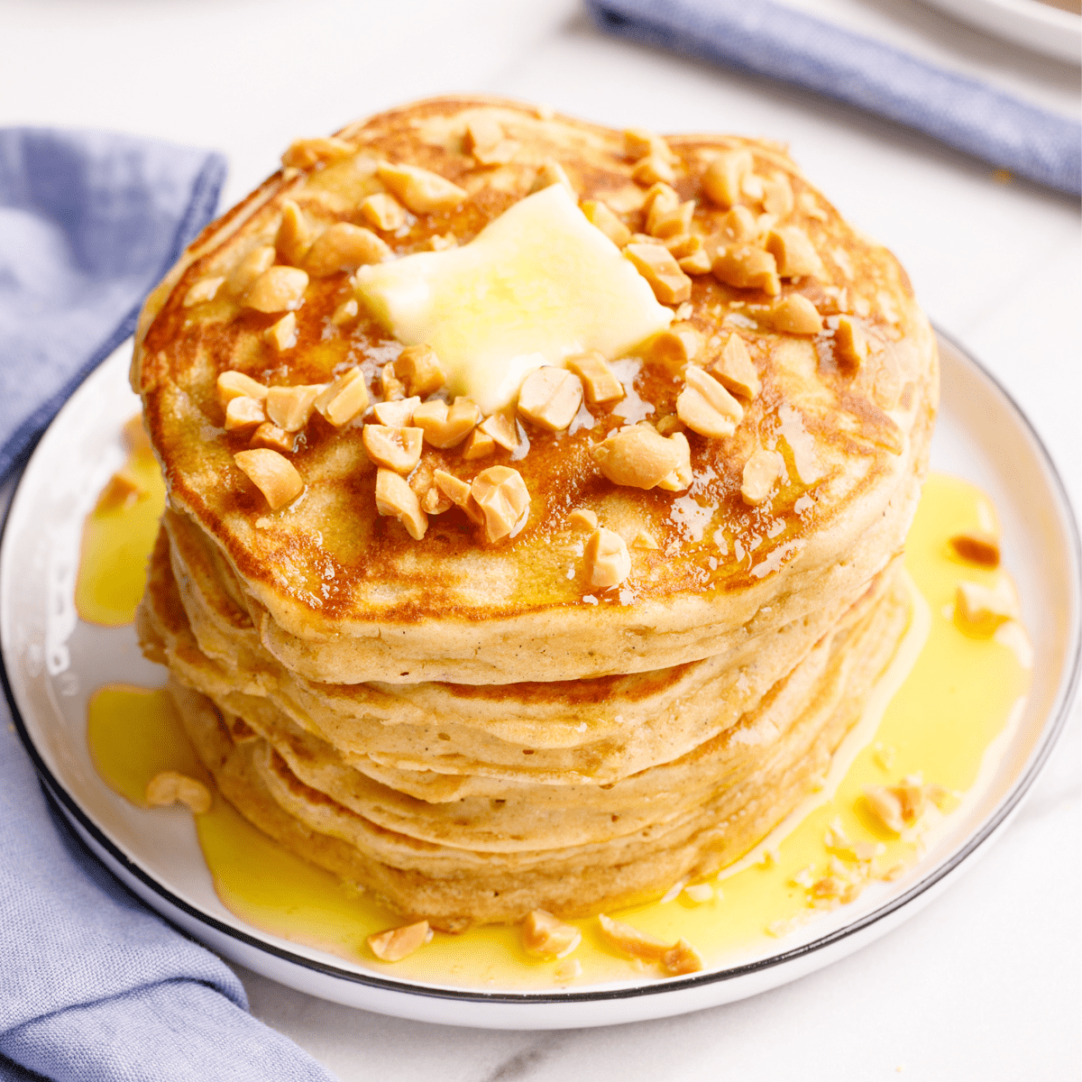 A stack of peanut butter pancakes topped with chopped peanuts and butter.