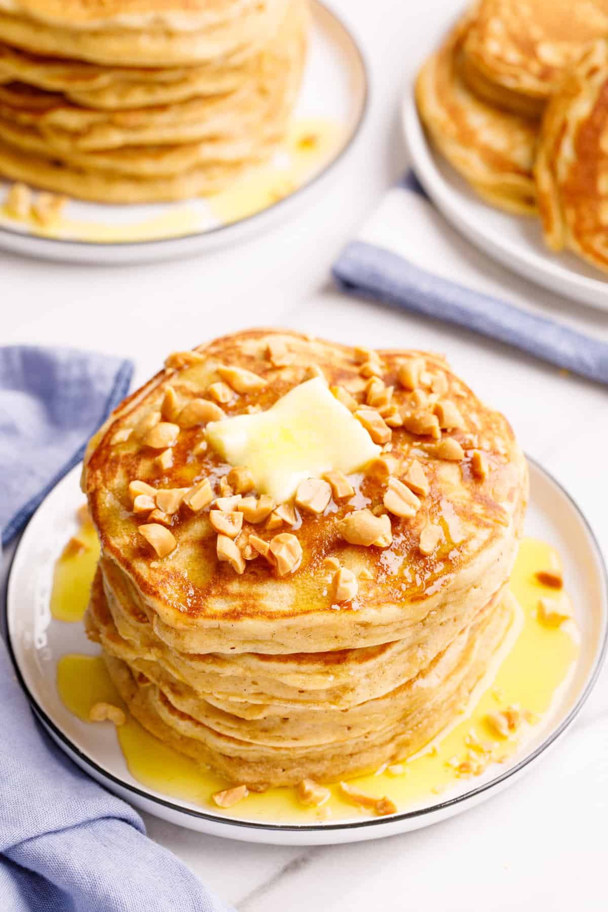 stack of four peanut butter pancakes topped with chopped peanuts, a tab of butter, and syrup