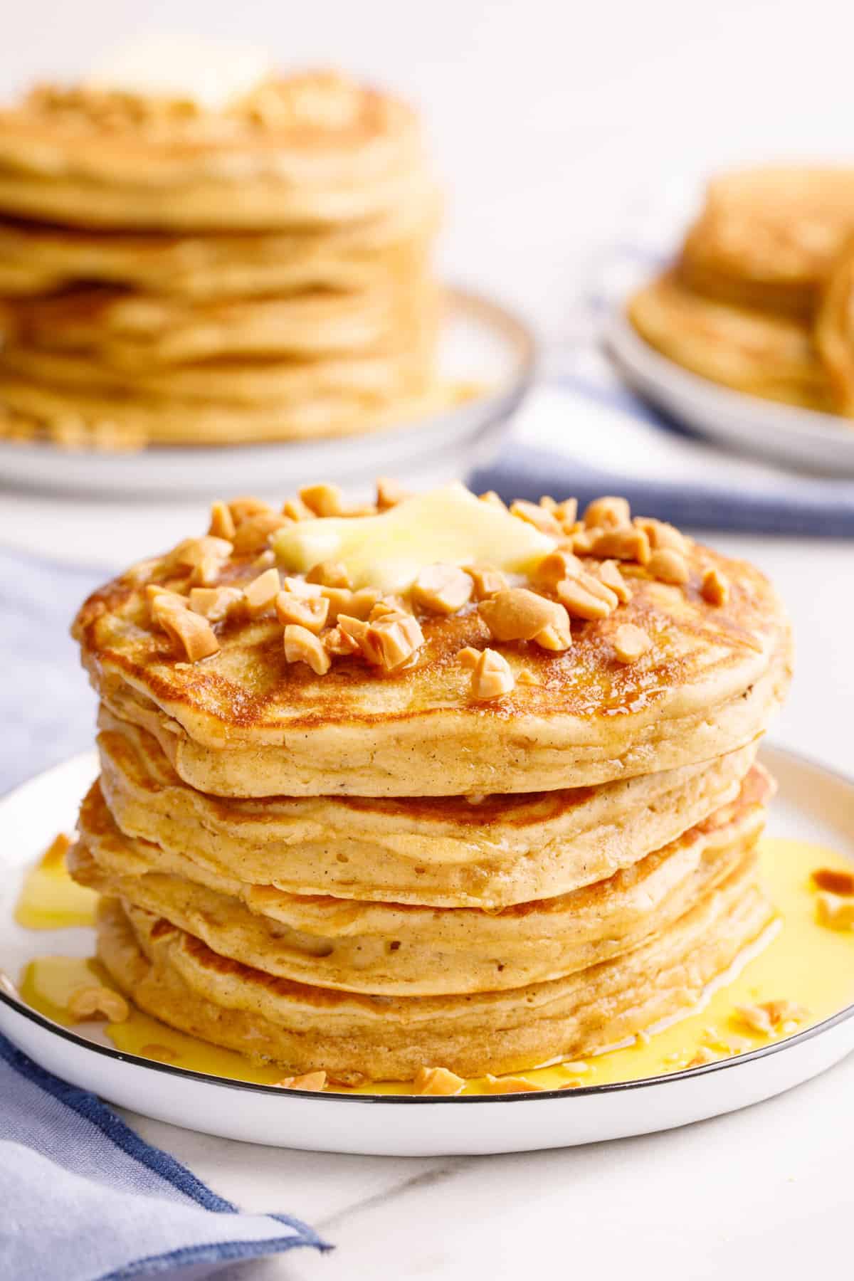stack of four peanut butter pancakes topped with chopped peanuts, a tab of butter, and syrup