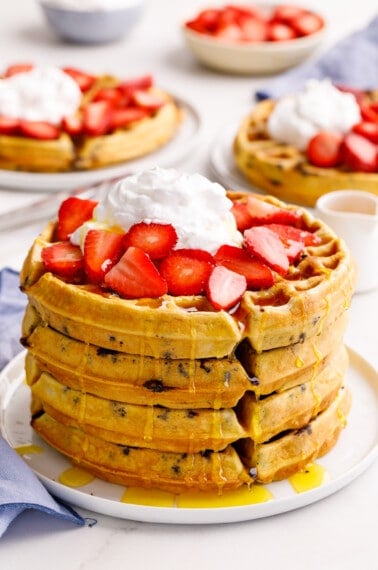 A stack of four chocolate chip waffles topped with strawberries and whipped cream.