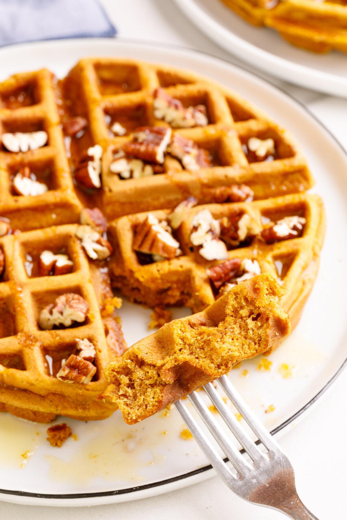 Sweet potato waffle on a plate with a bite taken out on a fork. 