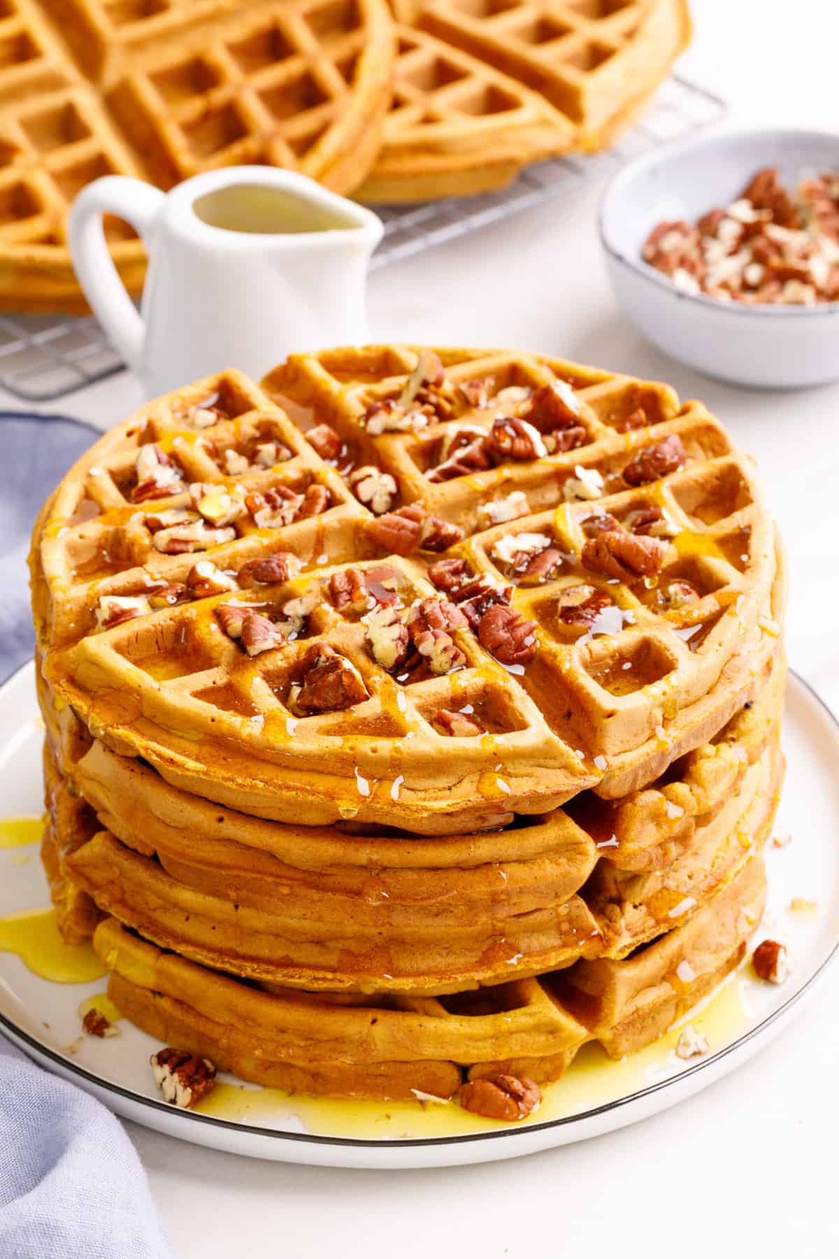 stack of four sweet potato waffles topped with chopped pecans and syrup served on a white round plate