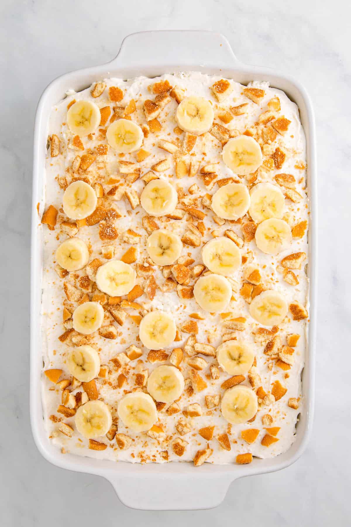top down image of banana pudding poke cake topped with fresh sliced bananas and nilla wafers