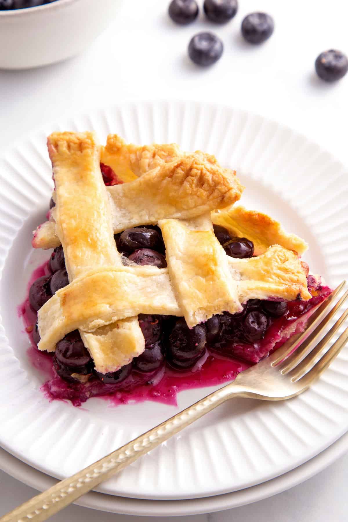 slice of blueberry pie sitting on a white round plate with a gold fork