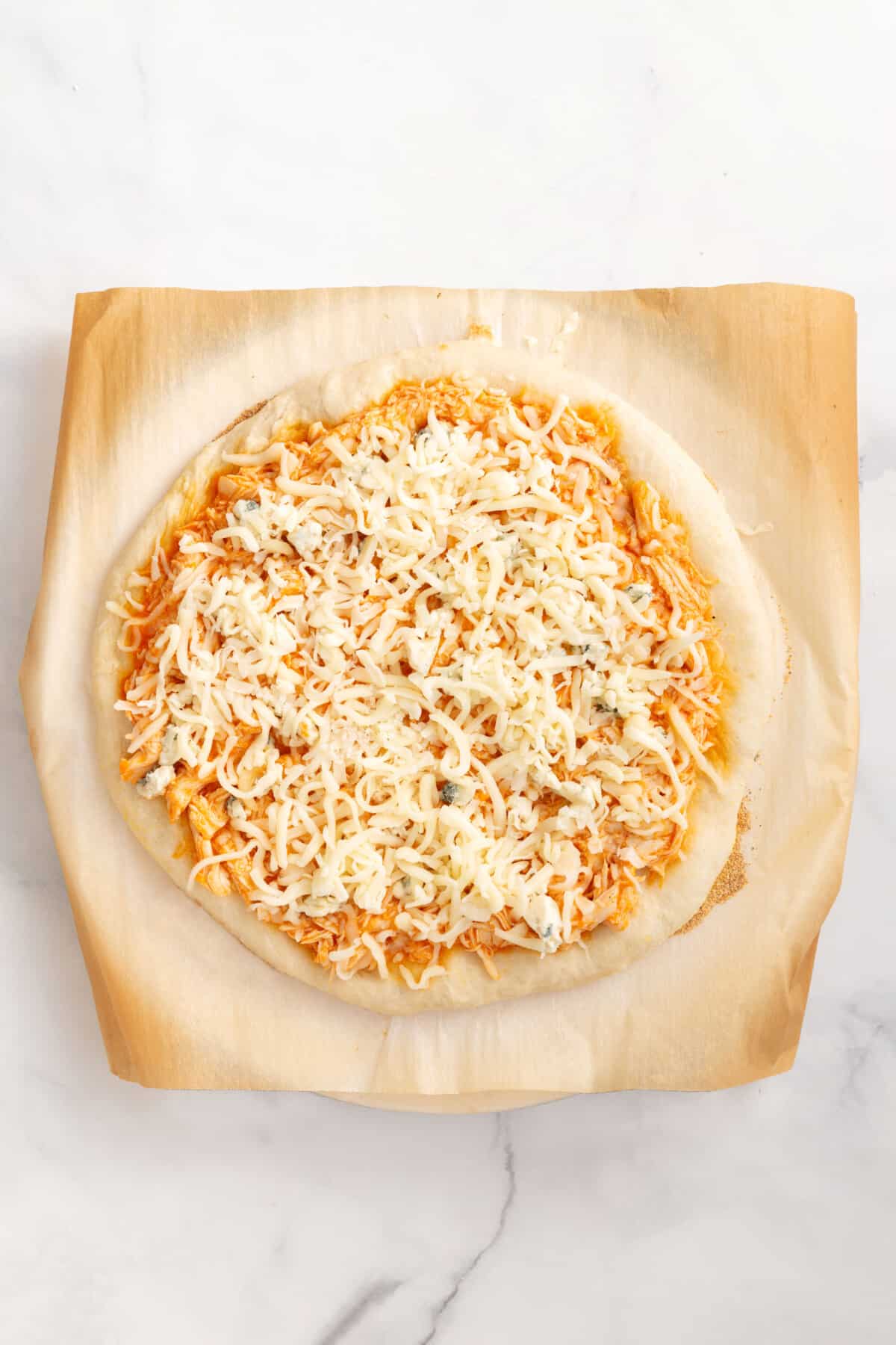 parbaked pizza crust with buffalo chicken mixture and shredded mozzarella cheese on top.