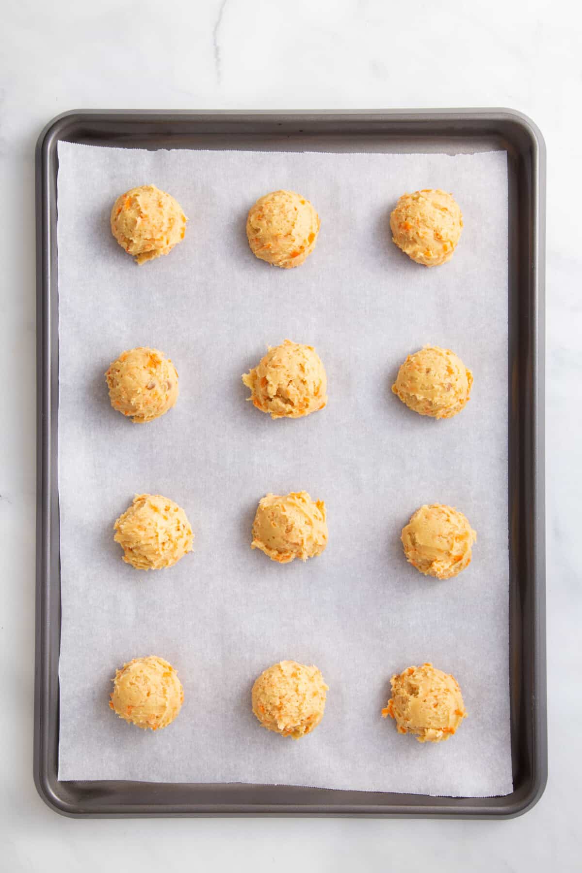 12 carrot cake cookie dough ball arranged on a parchment-lined baking sheet.