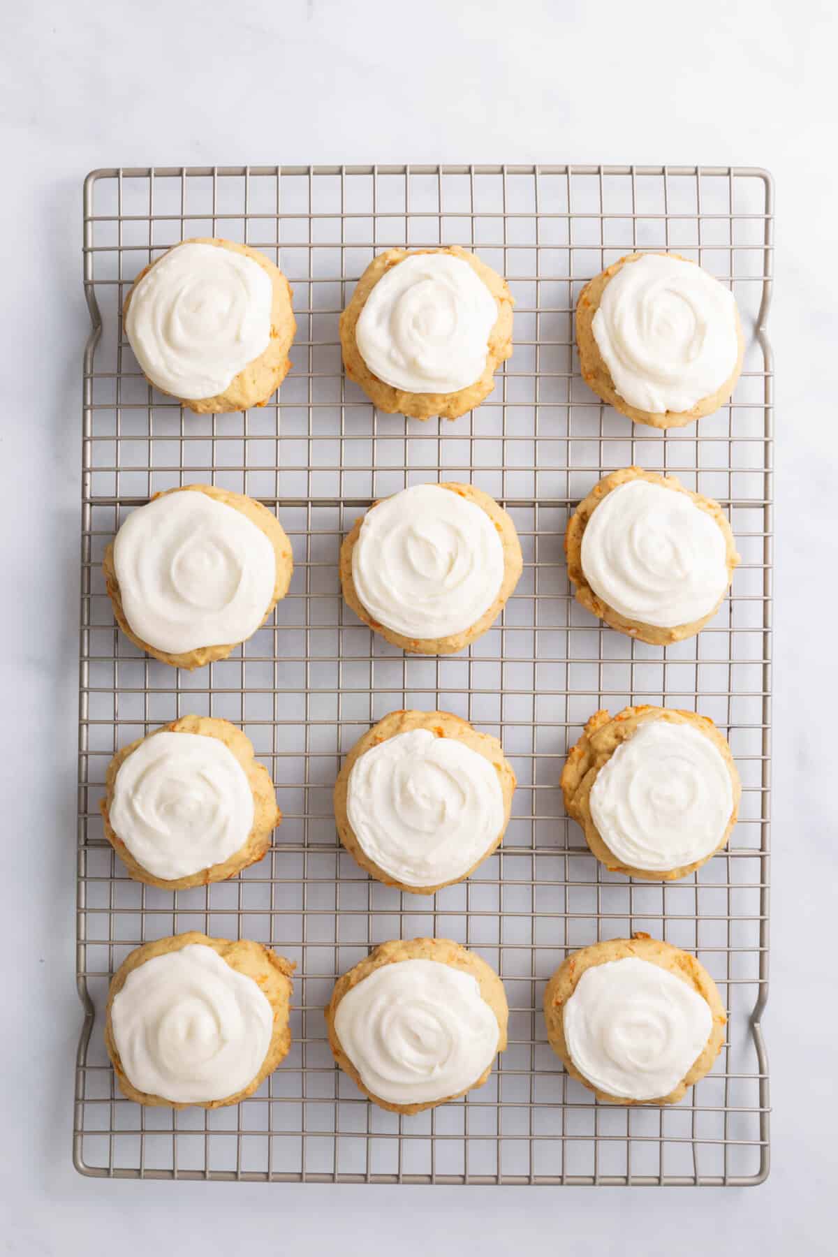 12 frosted carrot cake cookies sitting on a wire rack.