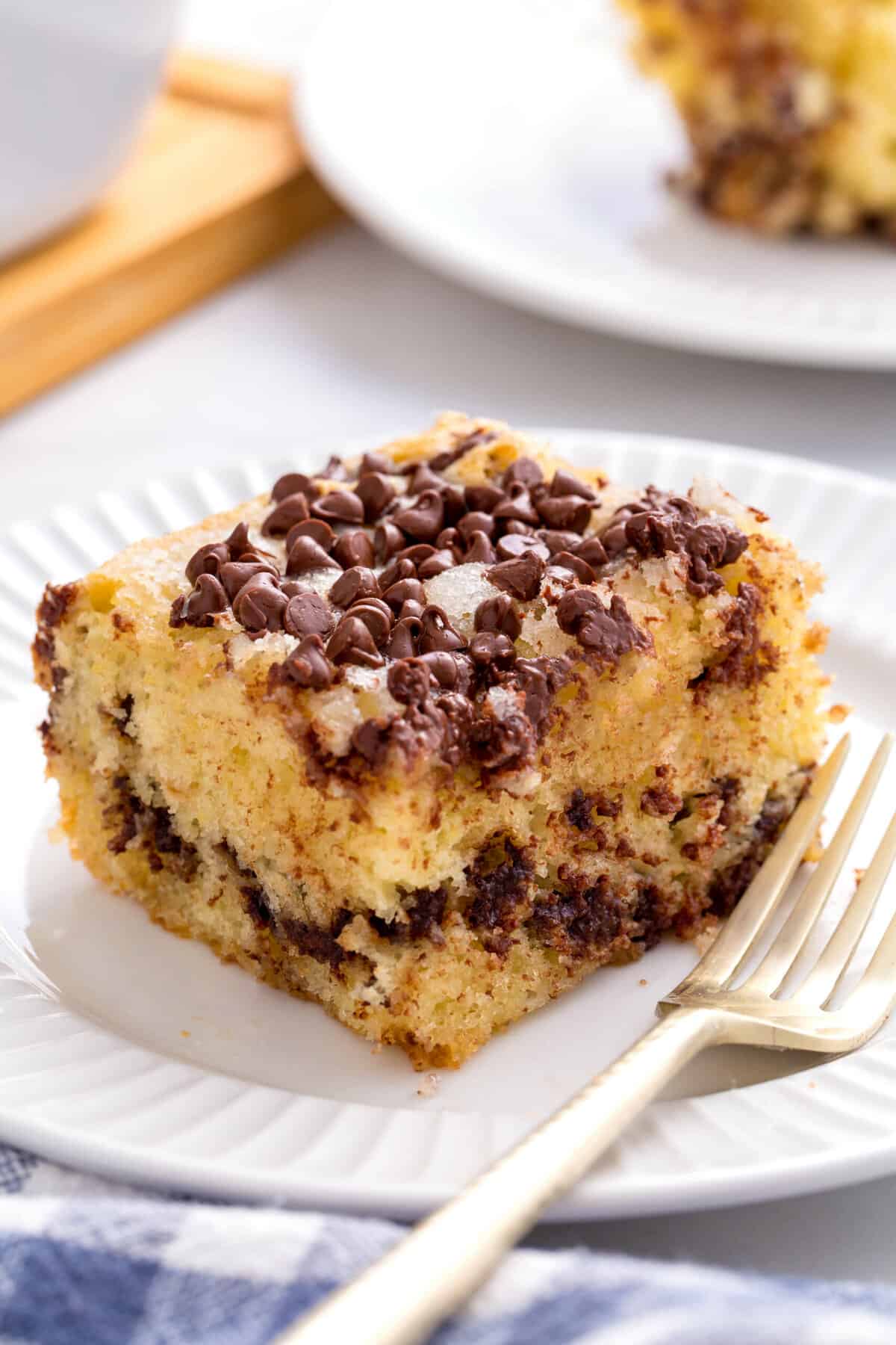 square slice of chocolate chip cake served on a white round plate with a gold fork
