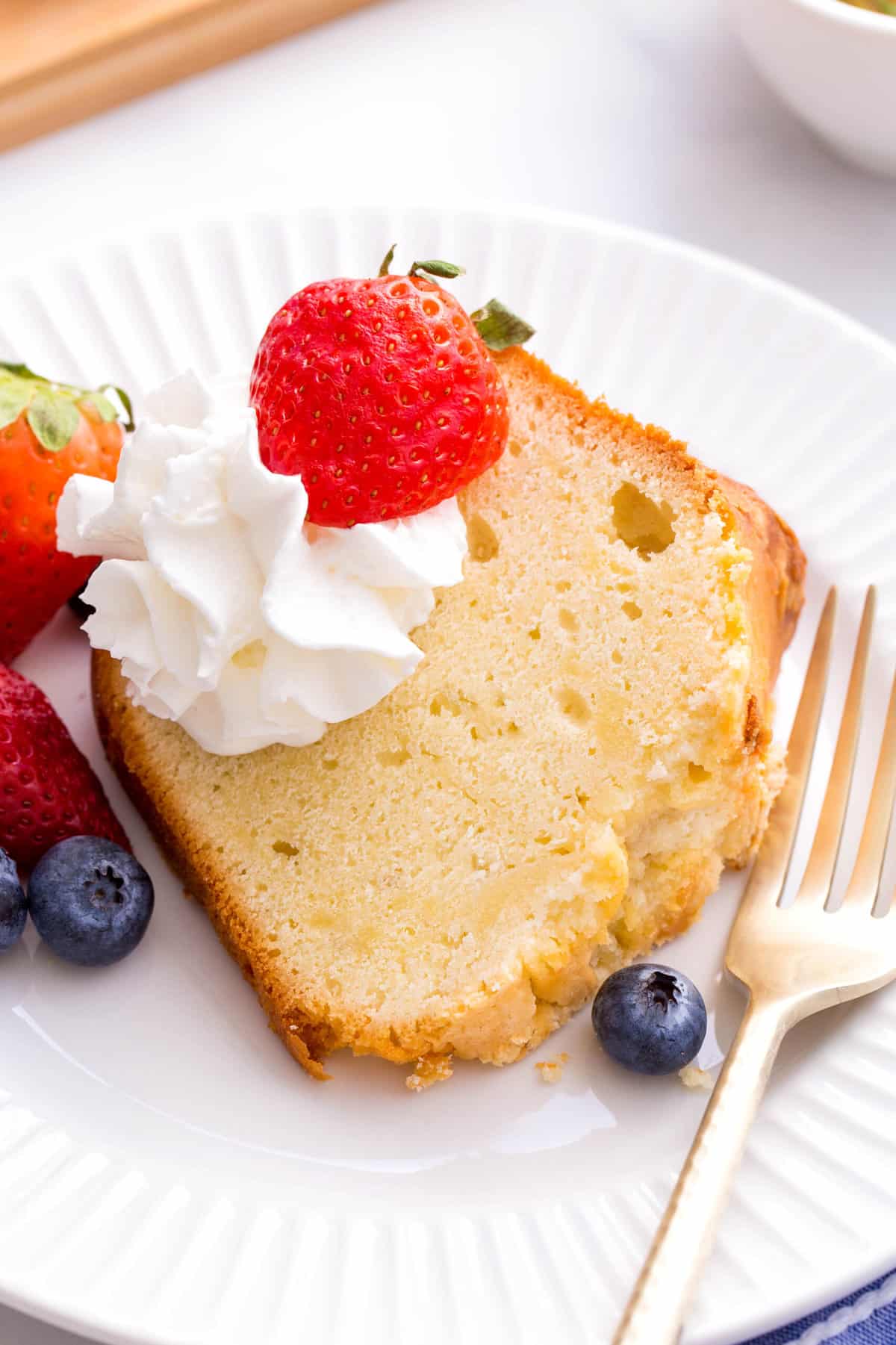 serving of cream cheese pound cake served on a white round plate topped with fresh berries and whipped cream