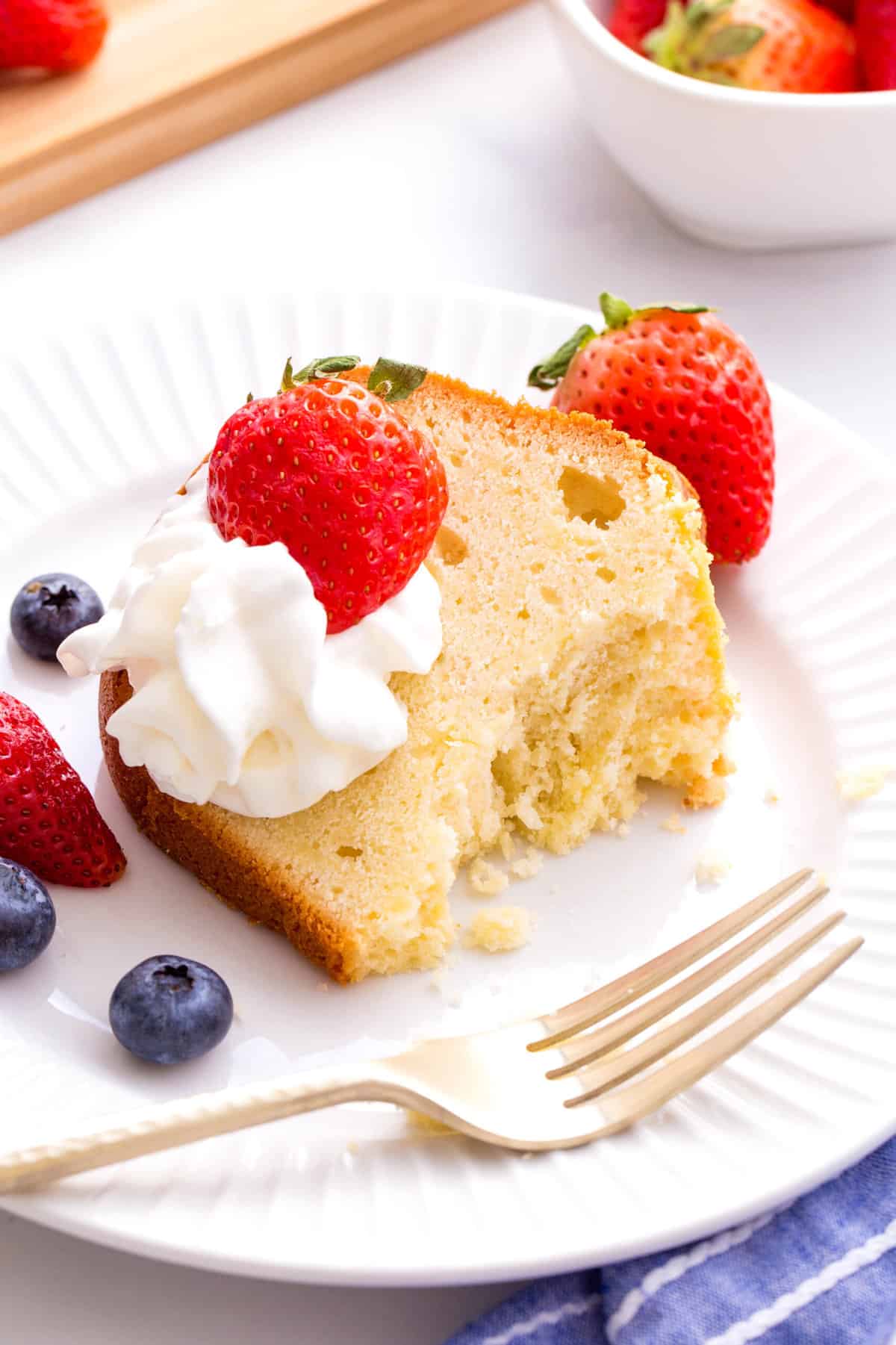 serving of cream cheese pound cake served on a white round plate topped with fresh berries and whipped cream