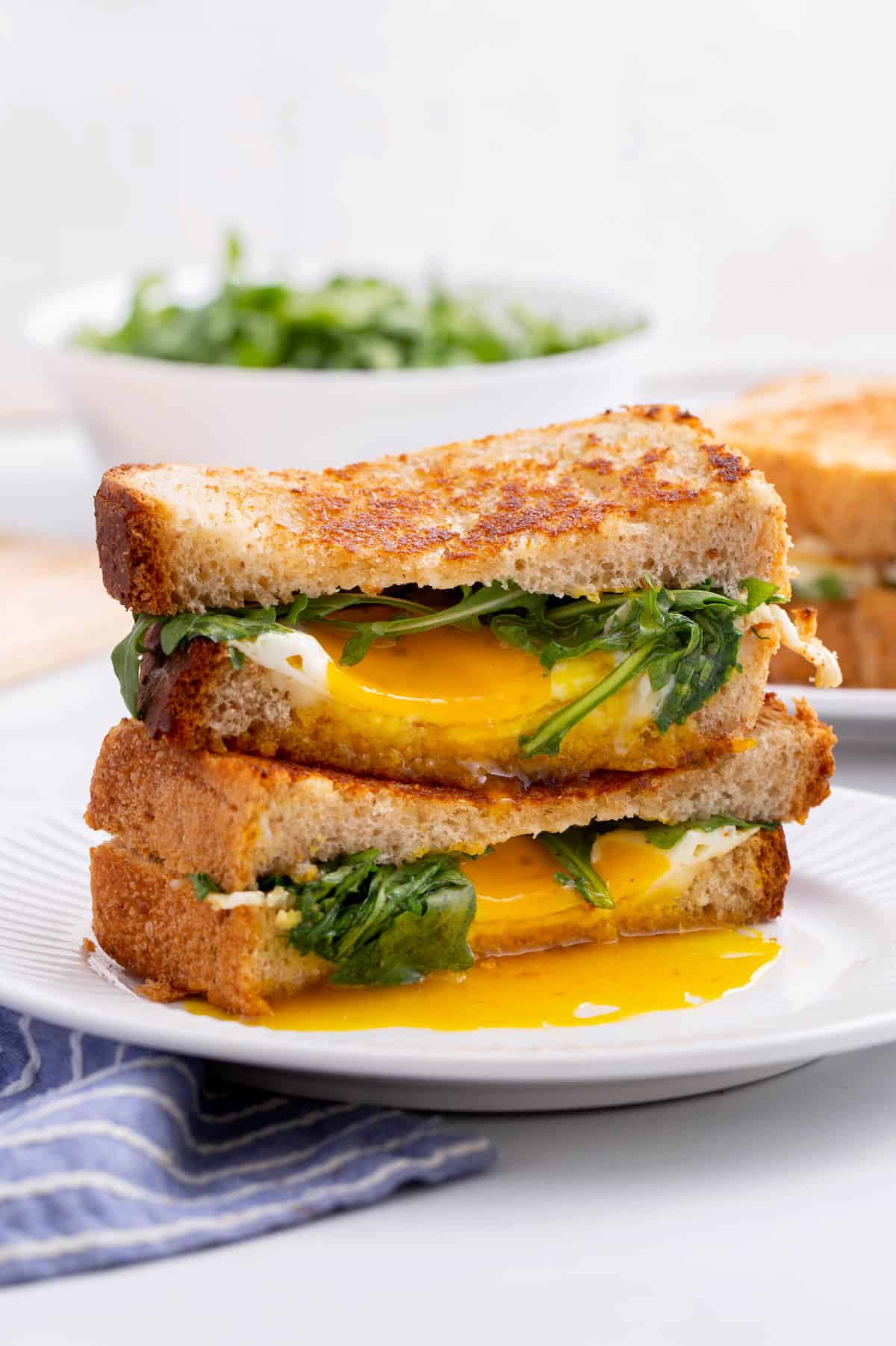 fried egg and cheese sandwich cut in half and stacked to show the cross section, sitting on a white round plate